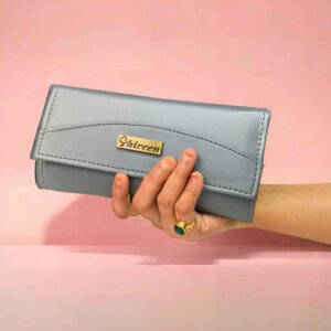 women's hand holding branded fancy clutch grey color, pink background color